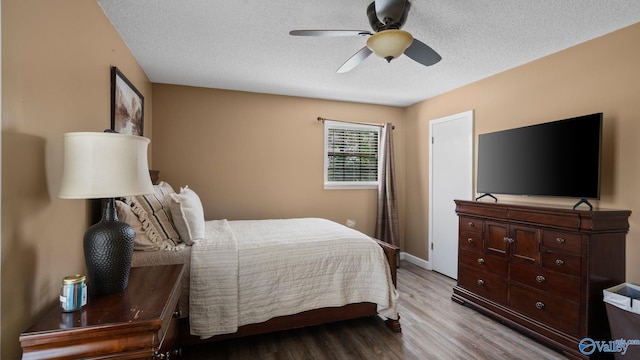bedroom featuring wood finished floors, a textured ceiling, a ceiling fan, and baseboards