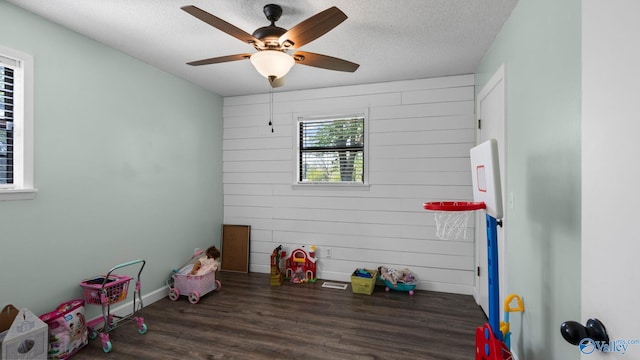 playroom with a textured ceiling, baseboards, wood walls, wood finished floors, and ceiling fan