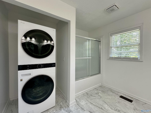 washroom with stacked washer / drying machine and a textured ceiling