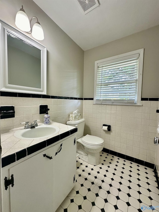 bathroom with vanity, vaulted ceiling, tile walls, and toilet