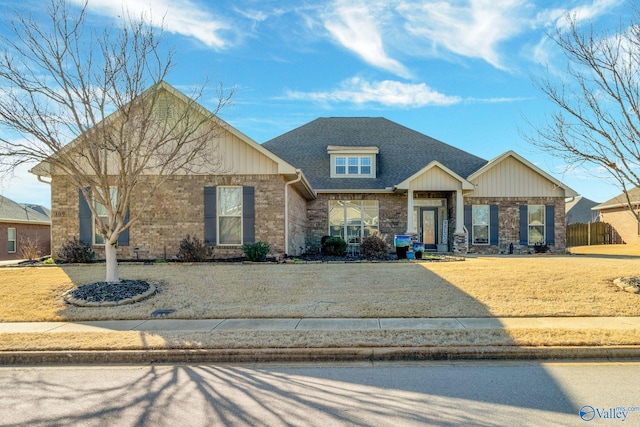 view of front of house with a shingled roof, a front yard, and brick siding