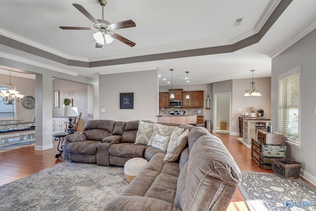 living room featuring crown molding, visible vents, a raised ceiling, and wood finished floors