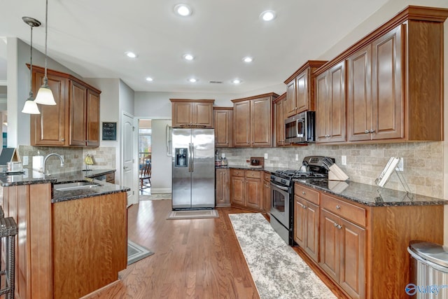 kitchen featuring dark stone counters, stainless steel appliances, brown cabinetry, and decorative light fixtures