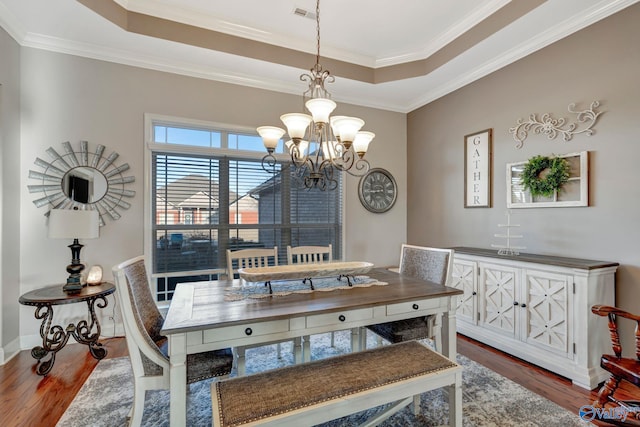 dining room with a tray ceiling, wood finished floors, visible vents, and an inviting chandelier