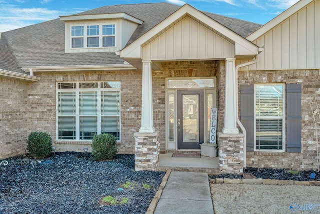 doorway to property featuring a shingled roof, board and batten siding, and brick siding