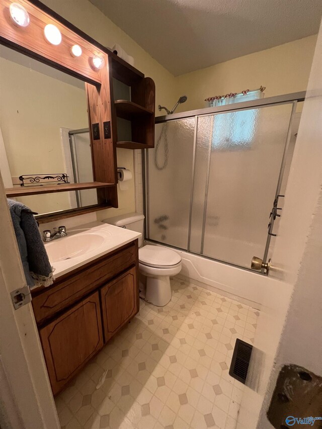 full bathroom featuring tile patterned flooring, bath / shower combo with glass door, a textured ceiling, toilet, and vanity