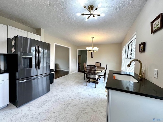 kitchen with sink, an inviting chandelier, white cabinetry, black refrigerator with ice dispenser, and pendant lighting