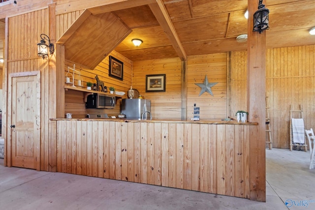 kitchen with wood walls, stainless steel appliances, concrete flooring, and decorative light fixtures