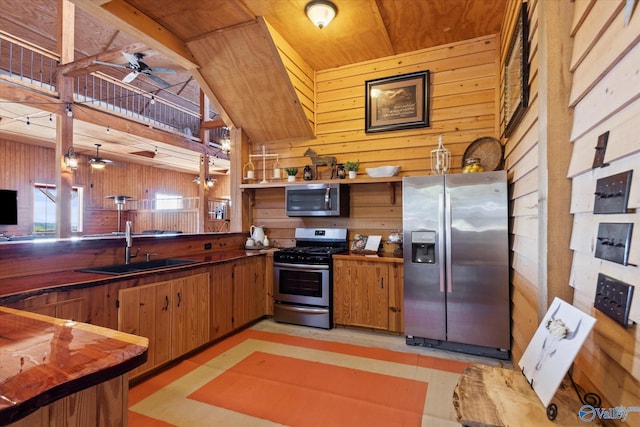 kitchen with ceiling fan, stainless steel appliances, sink, and wood walls