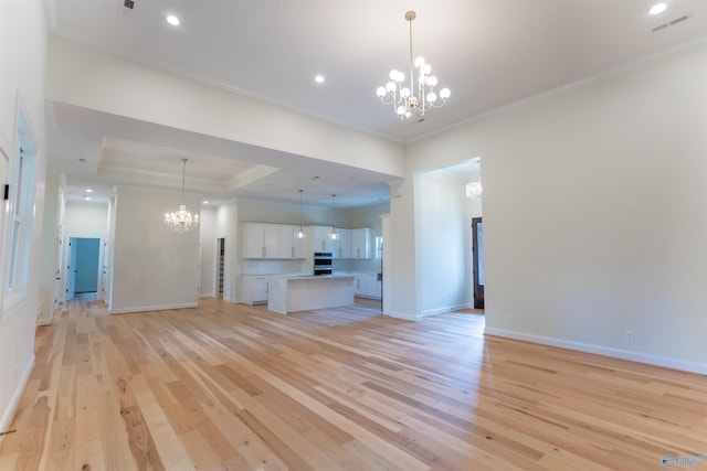 unfurnished living room featuring a chandelier, light wood-type flooring, a tray ceiling, and ornamental molding