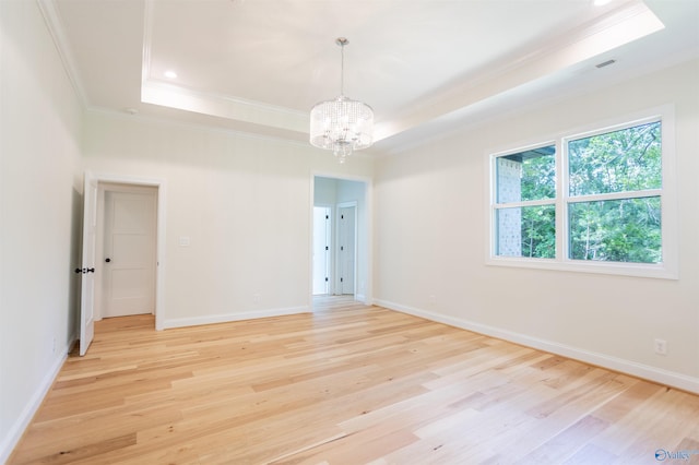 unfurnished room with an inviting chandelier, light wood-type flooring, crown molding, and a raised ceiling