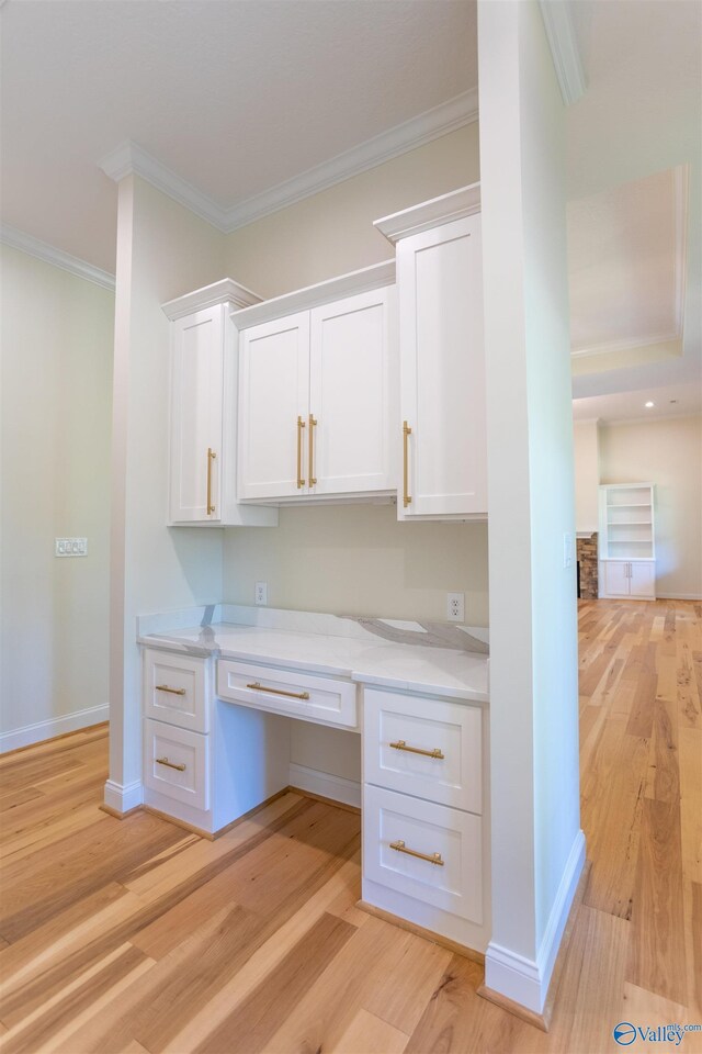 unfurnished office featuring light hardwood / wood-style flooring, built in desk, and ornamental molding