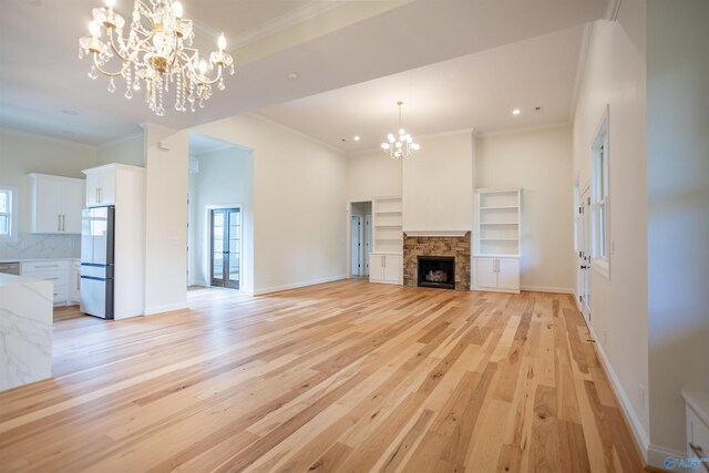 unfurnished living room with a stone fireplace, a chandelier, and light hardwood / wood-style floors