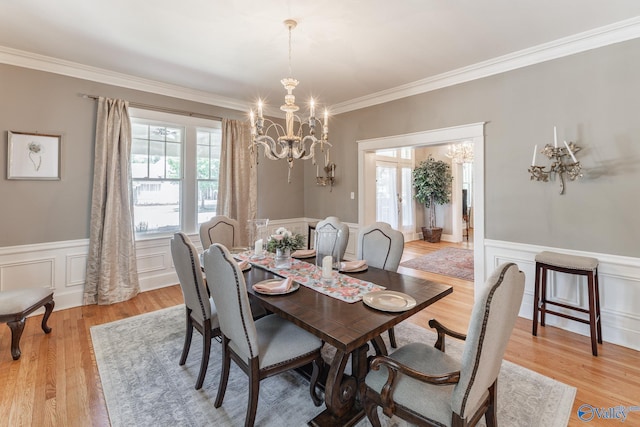 dining space with an inviting chandelier, crown molding, light wood-style floors, and wainscoting