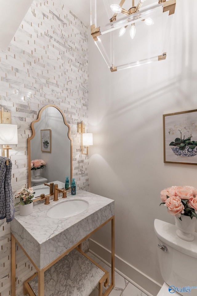 half bathroom with marble finish floor, toilet, vanity, and baseboards