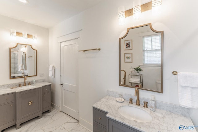 full bath with two vanities, baseboards, marble finish floor, and a sink