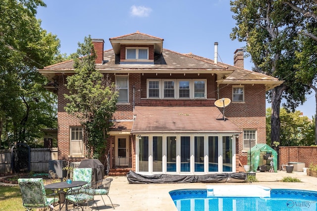 back of property featuring fence, a sunroom, a chimney, a patio area, and brick siding