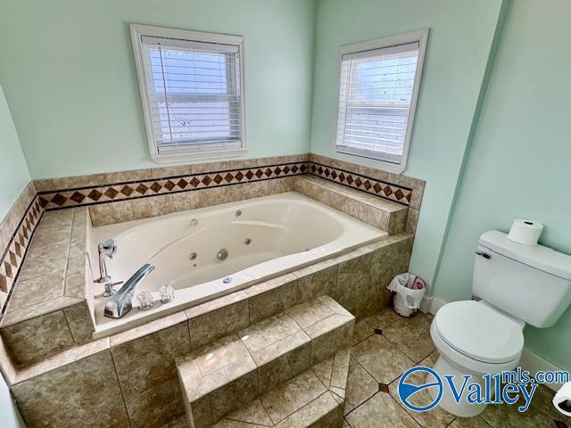 bathroom with tile patterned floors, toilet, and tiled bath