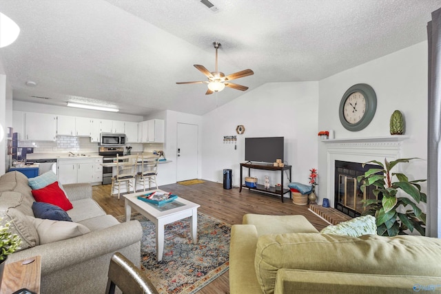 living room with vaulted ceiling, sink, ceiling fan, dark wood-type flooring, and a textured ceiling