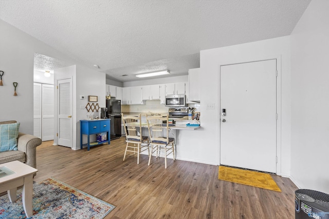 kitchen with white cabinetry, backsplash, black refrigerator, wood-type flooring, and kitchen peninsula