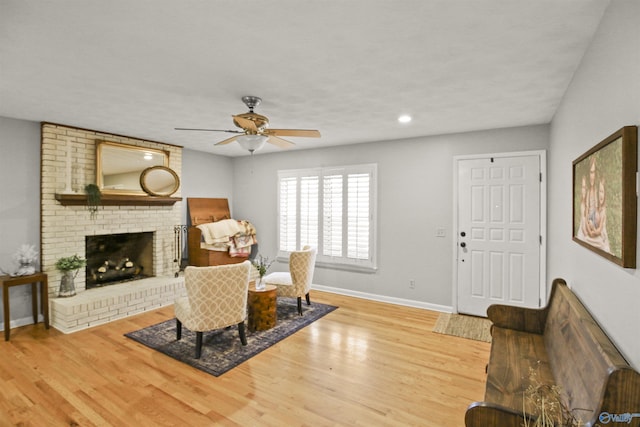 living room featuring ceiling fan, a brick fireplace, and light hardwood / wood-style flooring