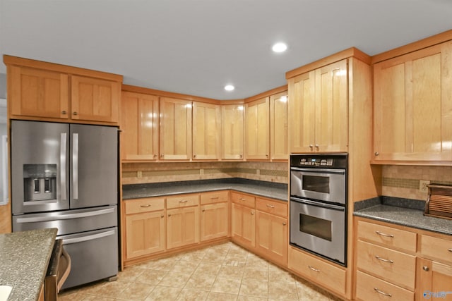 kitchen featuring stainless steel appliances, light brown cabinetry, light tile patterned floors, and backsplash