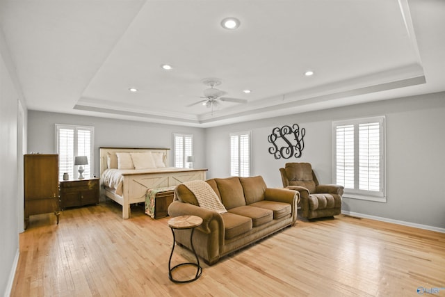 bedroom featuring ceiling fan, a tray ceiling, and light wood-type flooring