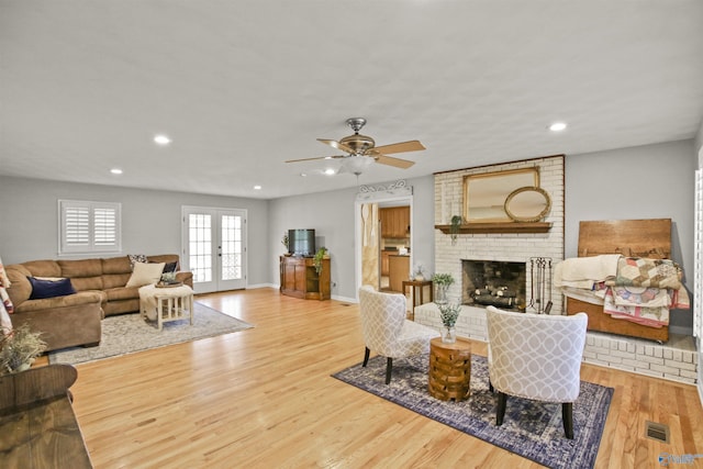 living room with french doors, ceiling fan, a fireplace, and light wood-type flooring