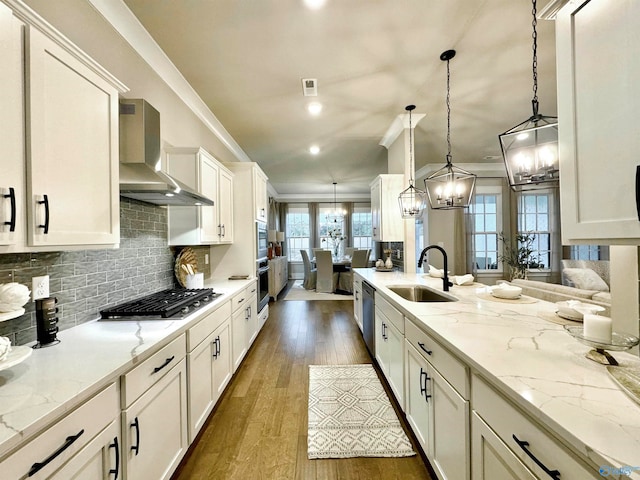 kitchen with wall chimney exhaust hood, sink, hanging light fixtures, and dark wood-type flooring