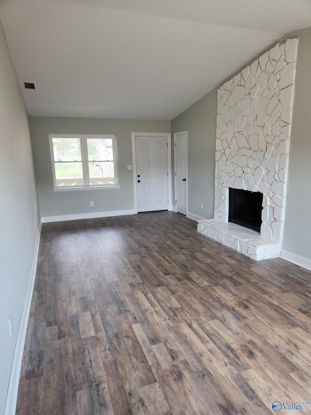 unfurnished living room featuring dark wood-style floors, a stone fireplace, baseboards, and visible vents