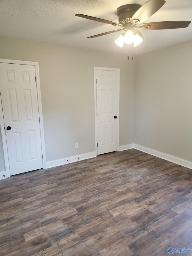 spare room featuring a textured ceiling, baseboards, dark wood-type flooring, and a ceiling fan