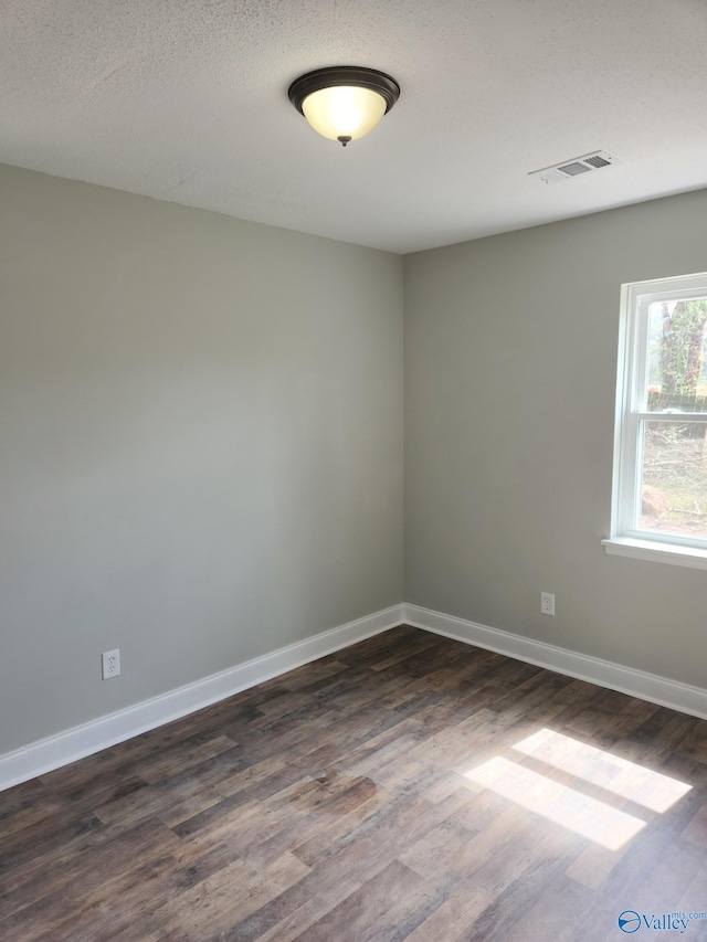 unfurnished room featuring visible vents, baseboards, a textured ceiling, and dark wood-style floors