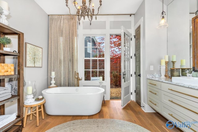 full bathroom featuring a soaking tub, vanity, an inviting chandelier, and wood finished floors