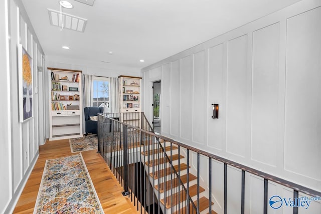 hall featuring an upstairs landing, a decorative wall, and light wood-type flooring