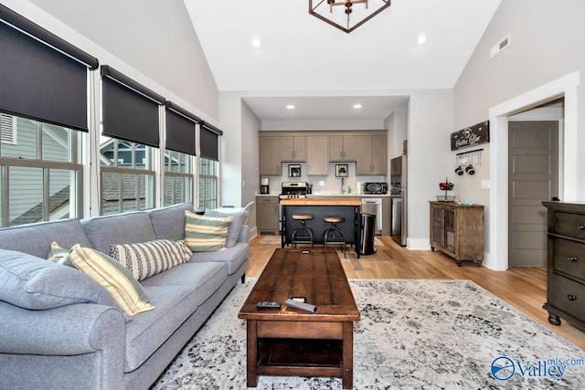 living room featuring recessed lighting, light wood-style floors, visible vents, and high vaulted ceiling