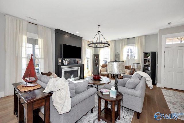 living room featuring visible vents, light wood finished floors, baseboards, a fireplace with raised hearth, and a notable chandelier