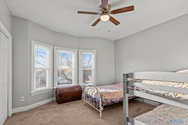 bedroom with a textured ceiling, a closet, light colored carpet, and ceiling fan