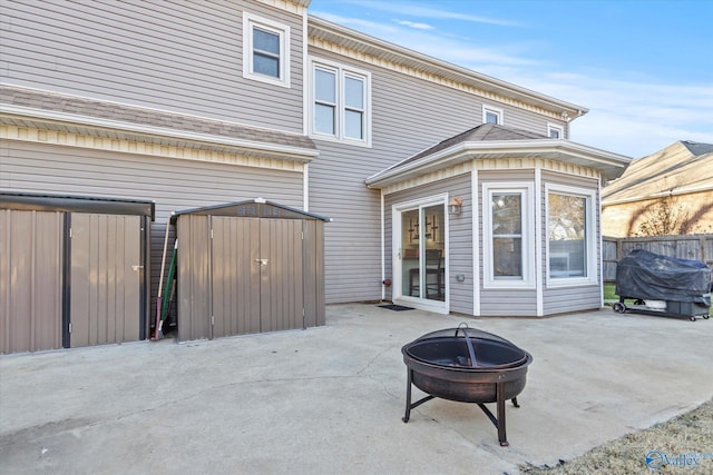 back of house with a fire pit, a patio, a storage shed, and an outbuilding