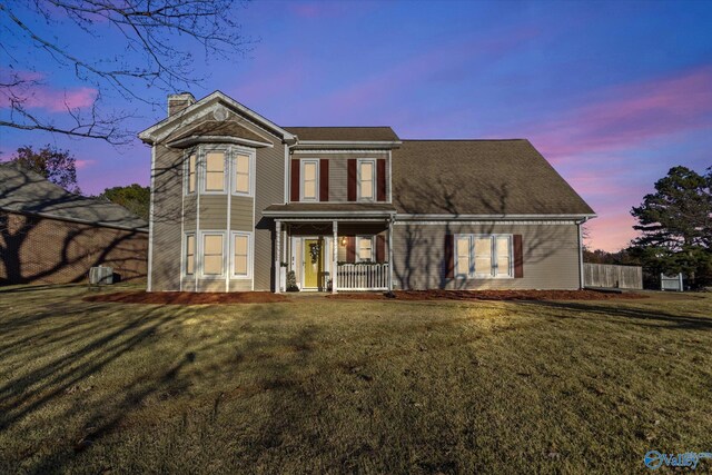 back of property at dusk featuring covered porch, a yard, and a chimney