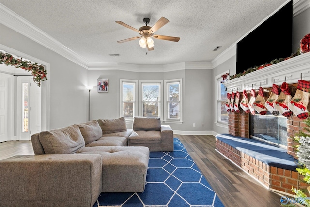 living room featuring a brick fireplace, a textured ceiling, ceiling fan, crown molding, and dark hardwood / wood-style floors