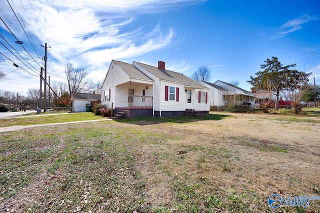 view of side of property with an outbuilding, covered porch, a lawn, and a chimney