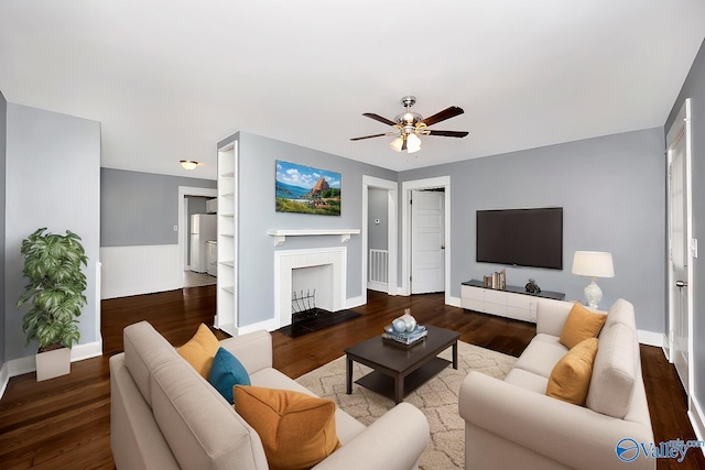 living room featuring a wainscoted wall, visible vents, a fireplace with flush hearth, ceiling fan, and wood finished floors