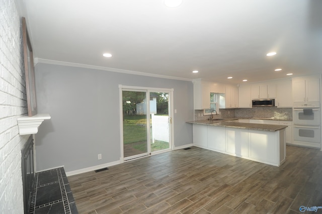 kitchen with stone countertops, white cabinetry, kitchen peninsula, sink, and dark wood-type flooring