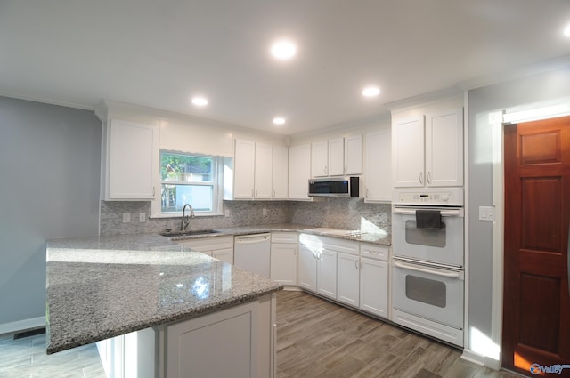 kitchen featuring white appliances, light hardwood / wood-style floors, kitchen peninsula, sink, and stone counters