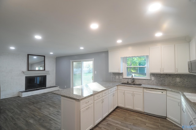 kitchen with white dishwasher, a brick fireplace, light stone counters, sink, and kitchen peninsula