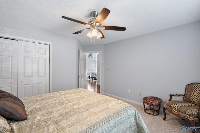 bedroom with carpet, a closet, a textured ceiling, baseboards, and ceiling fan with notable chandelier