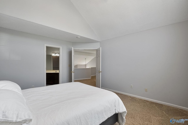 bedroom with lofted ceiling, dark carpet, ensuite bathroom, and baseboards