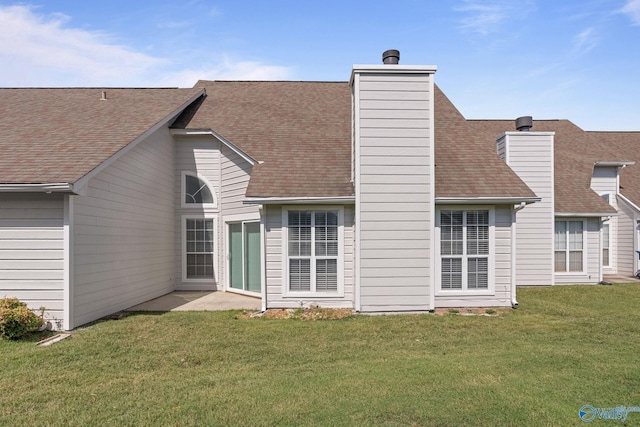 back of house with a shingled roof, a chimney, and a lawn