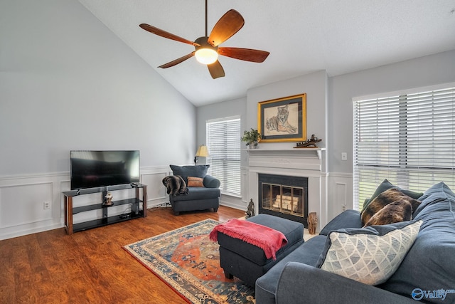 living room with a glass covered fireplace, wainscoting, lofted ceiling, and wood finished floors