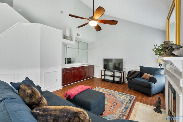 living area with lofted ceiling, a wainscoted wall, a fireplace with flush hearth, visible vents, and dark wood-style floors